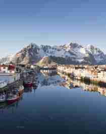 Houten huizen, vissersboten en besneeuwde bergen in Henningsvær op de Lofoten in Noord-Noorwegen op een zonnige winterdag