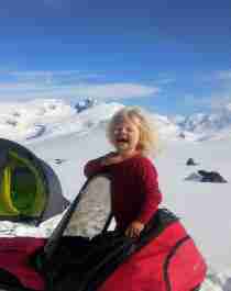 De 4 jaar oude Mina die in een skitrekker staat voor een tent op een zonnige winterdag in het nationaal park Jotunheimen, Oost-Noorwegen