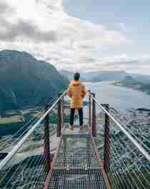 A person standing at the tip of Rampestreken viewpoint, looking out at the fjord and mountains of Åndalsnes in Northwest, Fjord Norway.