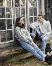 Two girls sitting on a bench outside, wearing woollen pullovers
