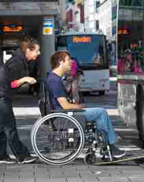 A man in a wheelchair is assisted on a bus