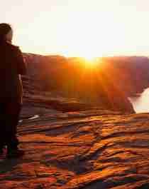 En person ser på soloppgangen fra Preikestolen i Ryfylke i Norge