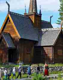 A group of people in old costumes walk past the stave church at Maihaugen in Lillehammer, Eastern Norway