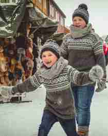 Two smiling children next to the stalls at Røros Christmas Market in Trøndelag, Norway