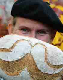A man is holding up a bread with flour designed as a moustache in Norway