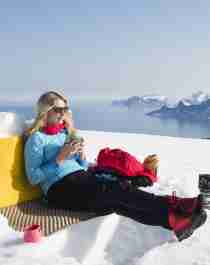 En kvinna som tar en paus i solen på vintervandring till Ryten i Lofoten, Nord-Norge