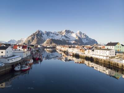 Wooden houses, fishing boats and snowcapped mountains, Henningsvær in certified Sustainable Destination Lofoten, Northern Norway