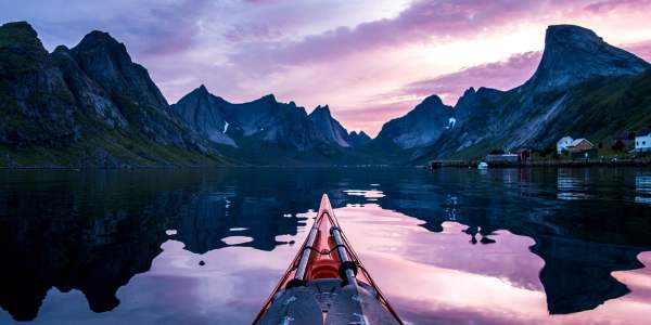 The tip of a kayak and steep mountains in the midnight sun in Lofoten, Northern Norway