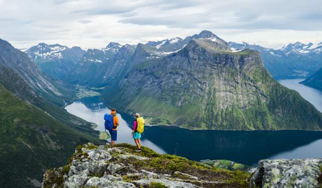 Una pareja disfruta de las vistas del fiordo Hjørundfjord desde lo alto de una montaña.