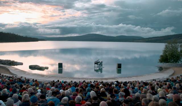 A pianist playing the grand piano on the Gålåvatnet lake, in front of an audience. The Peer Gynt Festival, Norway