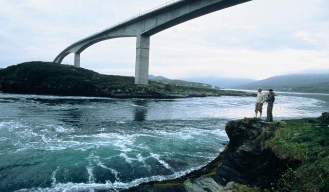 To personer står på et utsiktspunkt til Saltstraumen, langs vannkanten, i Nord-Norge.
