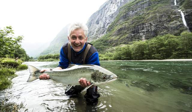 En sportsfisker står i Nærøydalselva på Vestlandet og holder opp en stor laks