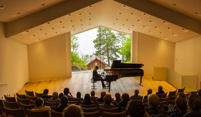 Man playing the piano in front of an audience at the Troldsalen room at Edvard Grieg Museum Troldhaugen in Bergen, Norway