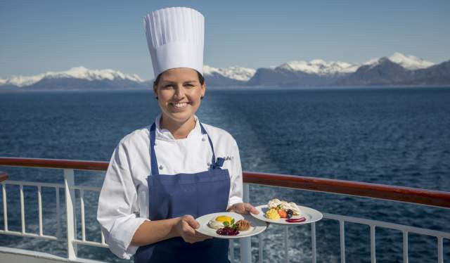 A female chef standing on the deck of a Hurtigruten ship with two plates of food