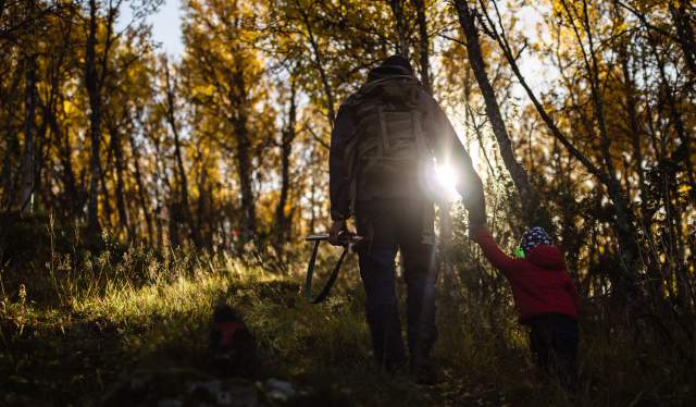 En far holder sin sønn i hånden mens de går gjennom skogen med høstsolen skinnende inn mellom grenene