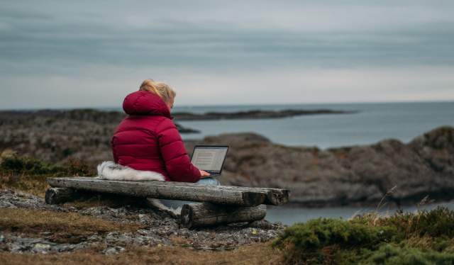 A woman sitting outdoors with her computer in Solund in Fjord Norway