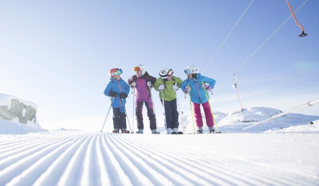 Four kids with skiers stand on a freshly groomed slope next to a button lift in Hemsedal, Eastern Norway