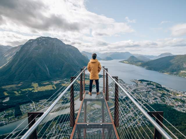 A person standing at the tip of Rampestreken viewpoint, looking out at the fjord and mountains of Åndalsnes in Northwest, Fjord Norway.