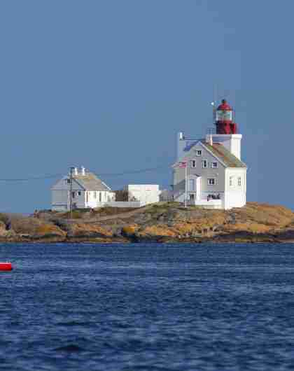 A sailboat passing by the Lyngør lighthouse during summer in Southern Norway.