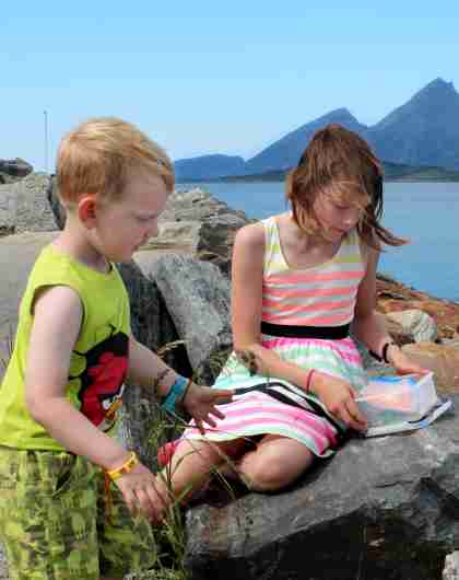 Two kids sitting on rocks next to the sea and try geocaching in Sandnessjøen in Nordland, Northern Norway