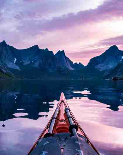 The tip of a kayak and steep mountains in the midnight sun in Lofoten, Northern Norway