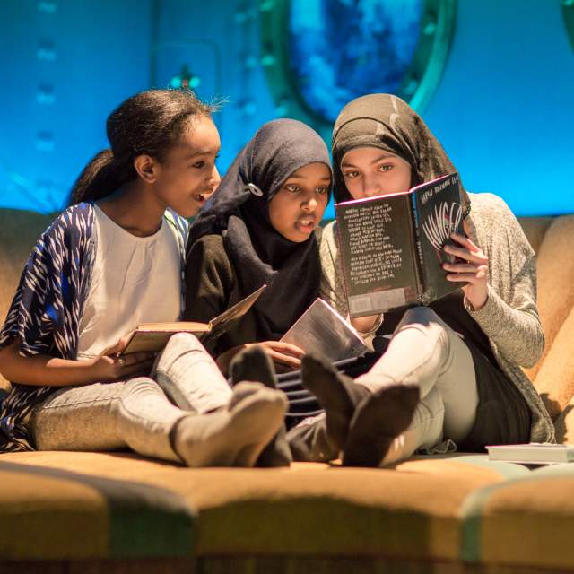 Three girls reading a book in the Biblo Tøyen library, Oslo, Eastern Norway