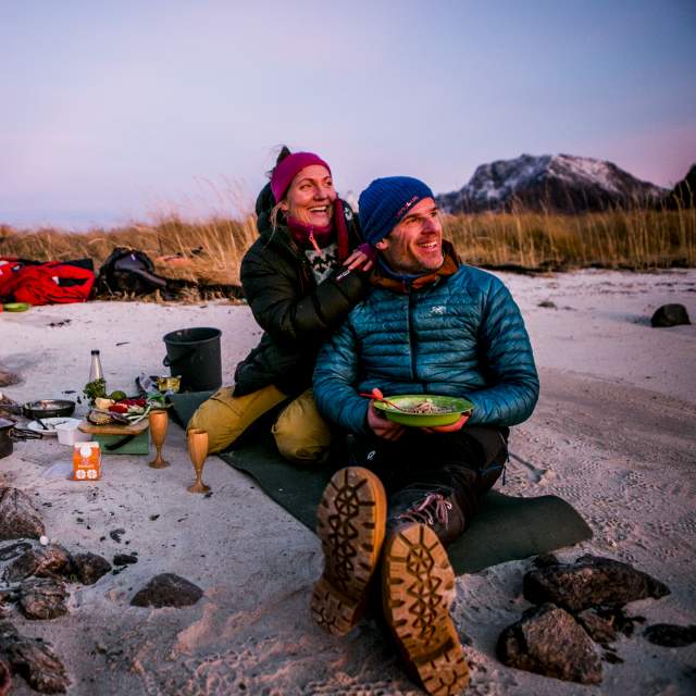 Två campare som har en mysig grillmiddag på stranden i kvällssol