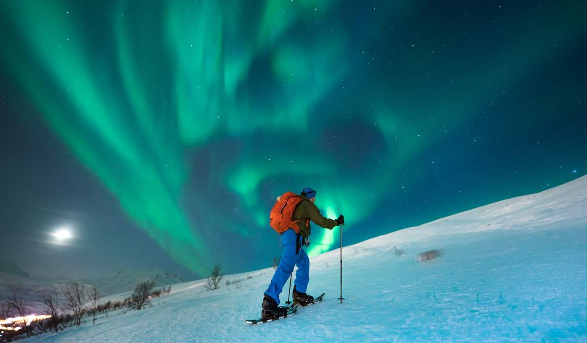 A person snowshoeing under the northern lights in Tromsø, Northern Norway
