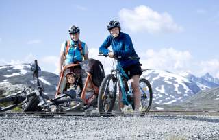 A family of three with e-bikes on a road near Åndalsnes, Fjord Norway