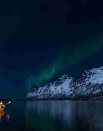 A woman paddling under the northern lights in Lofoten