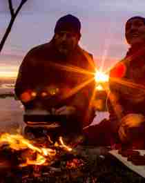 People cooking a meal outdoors over open fire during sunset