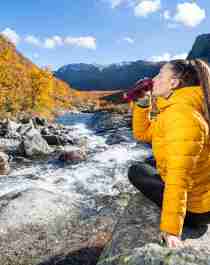 Woman drinking water from a river, Hemsedal, Norway.