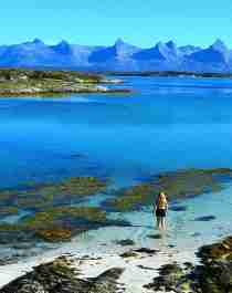 A woman standing in the sea on Herøy island with a view of The seven sisters mountain range on Helgelandskysten, Norway