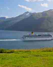 A cruise ship is driving through Innfjorden with mountains and green fields on both sides