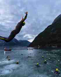 A person in wetsuit jumping into the fjord in Northern Norway as part of the Norseman competition