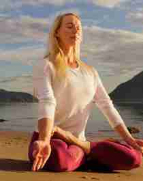 Ei dame sitter i lotusstilling å gjør yoga på stranden i midnattsolen i Nord-Norge
