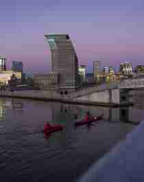 Two people in kayaks in front of the new Deichman main library in Oslo in a purple sunset