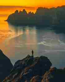 A man standing on the tip of a mountain in the midnight sun at Senja
