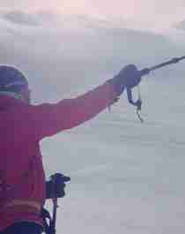 To mennesker i vinterklær peker med en stav mot snødekt fjell