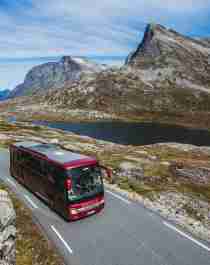 En buss kjører forbi en innsjø på en solfylt dag på nordvestlandet