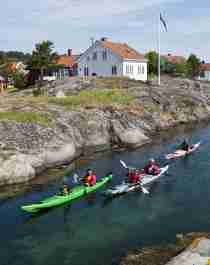 Drei Kajaks durchqueren eine Meeresstraße zwischen den Inseln von Risør, Südnorwegen
