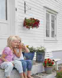 Two young girls talking while sitting on the stone steps in front of a white wooden house in Loshavn, Farsund, Southern Norway.