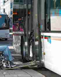 En mann i rullestol får hjelp til å komme seg inn på en buss