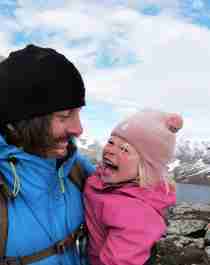 En lille pige og hendes far smiler og krammer hinanden på en vandretur ved Hjørundfjorden i Fjord Norge