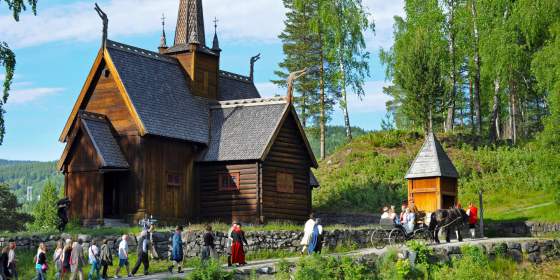 A group of people in old costumes walk past the stave church at Maihaugen, Lillehammer