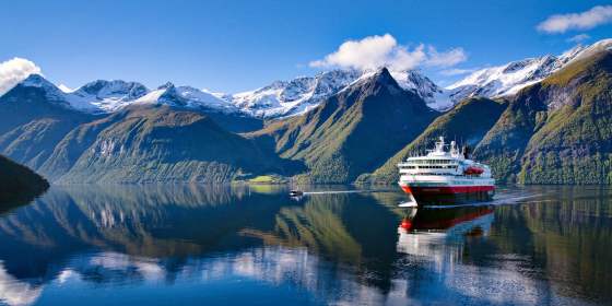 A Hurtigruten ship on the Hjørundfjord in Fjord Norway surrounded by snow-clad mountains