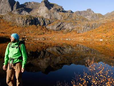 A man standing by a lake in the mountains with autumn colors all around