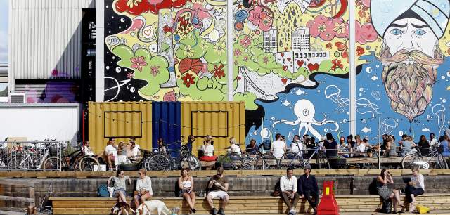 People sitting in front of a wall with street art at Vippa food court in Oslo, Norway