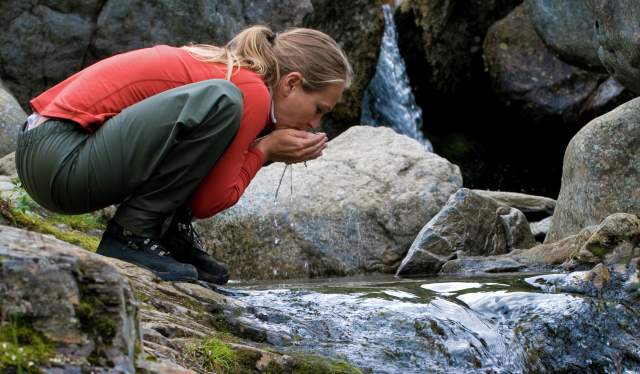 En dame drikker vann fra en fjellbekk