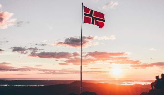 The Norwegian flag and a couple enjoying the sunset on a mountain top